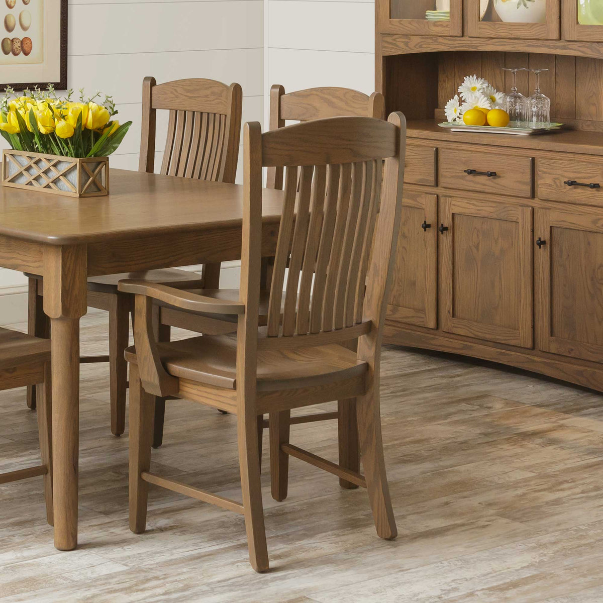 Oak arm chair viewed from behind at a dining table, with a matching oak hutch in the background