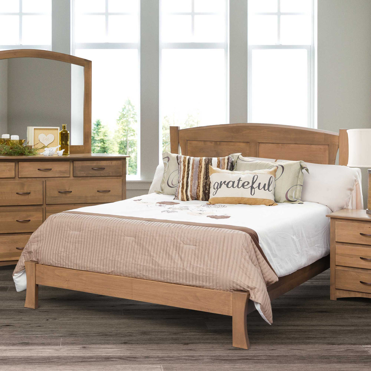 Arched panel bed in light natural wood with a low footboard, styled with striped and script accent pillows