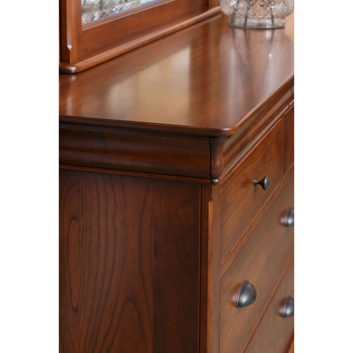 Close-up of the cherry dresser's rounded top corner, molded edge and antiqued cup pulls with the mirror behind