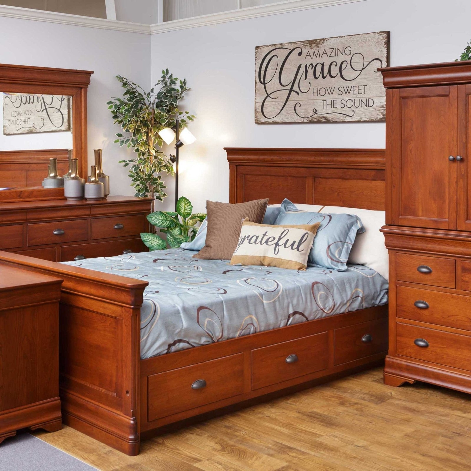 Cherry bedroom suite in a showroom with a storage sleigh bed, nightstand, dresser with mirror and armoire