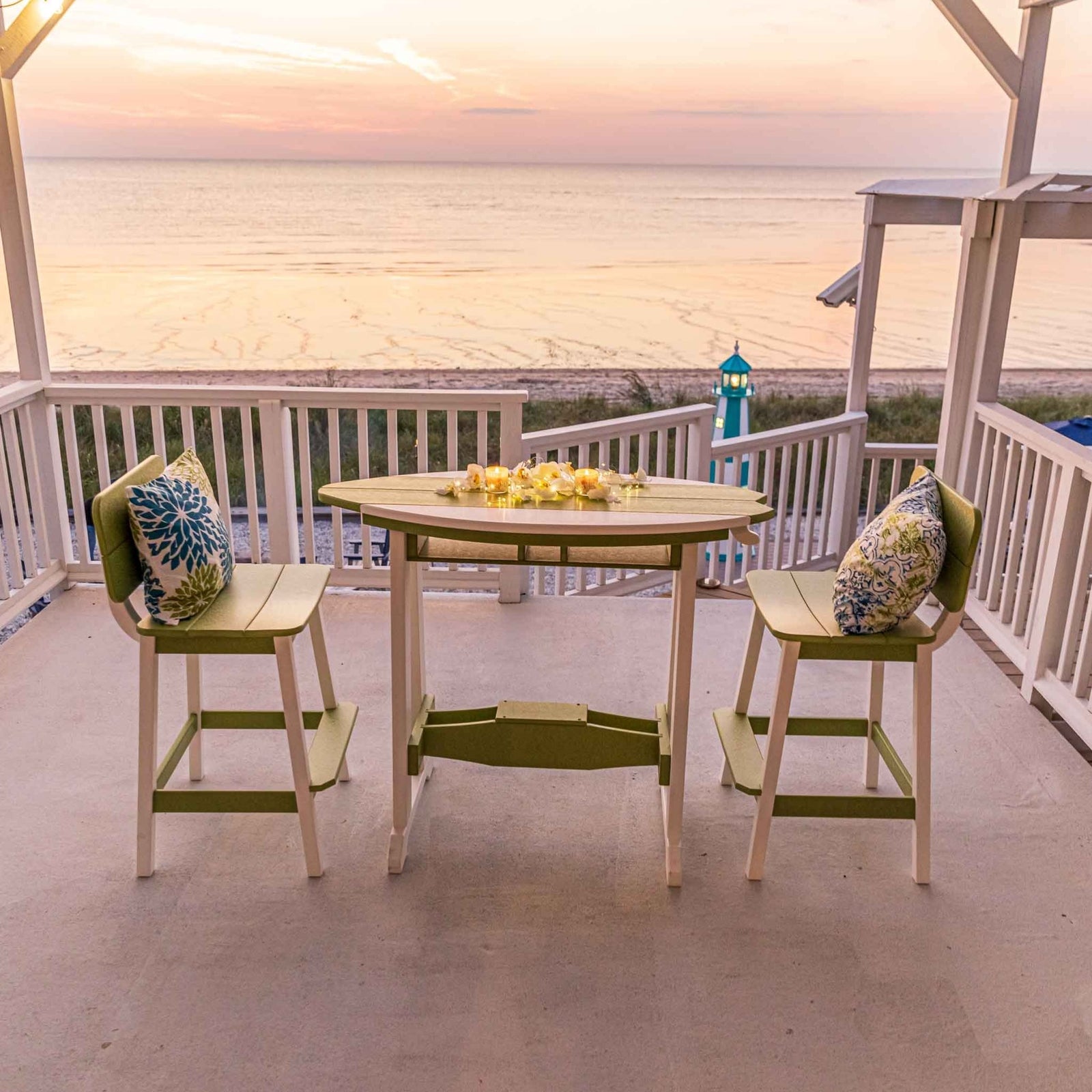 Lime green and white surfboard shaped counter table with two bar chairs on an oceanfront porch at sunset