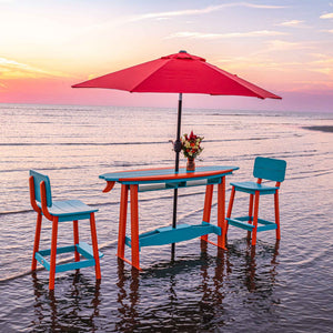 Turquoise and orange poly surfboard bar table set for two with red patio umbrella at sunset on the shore