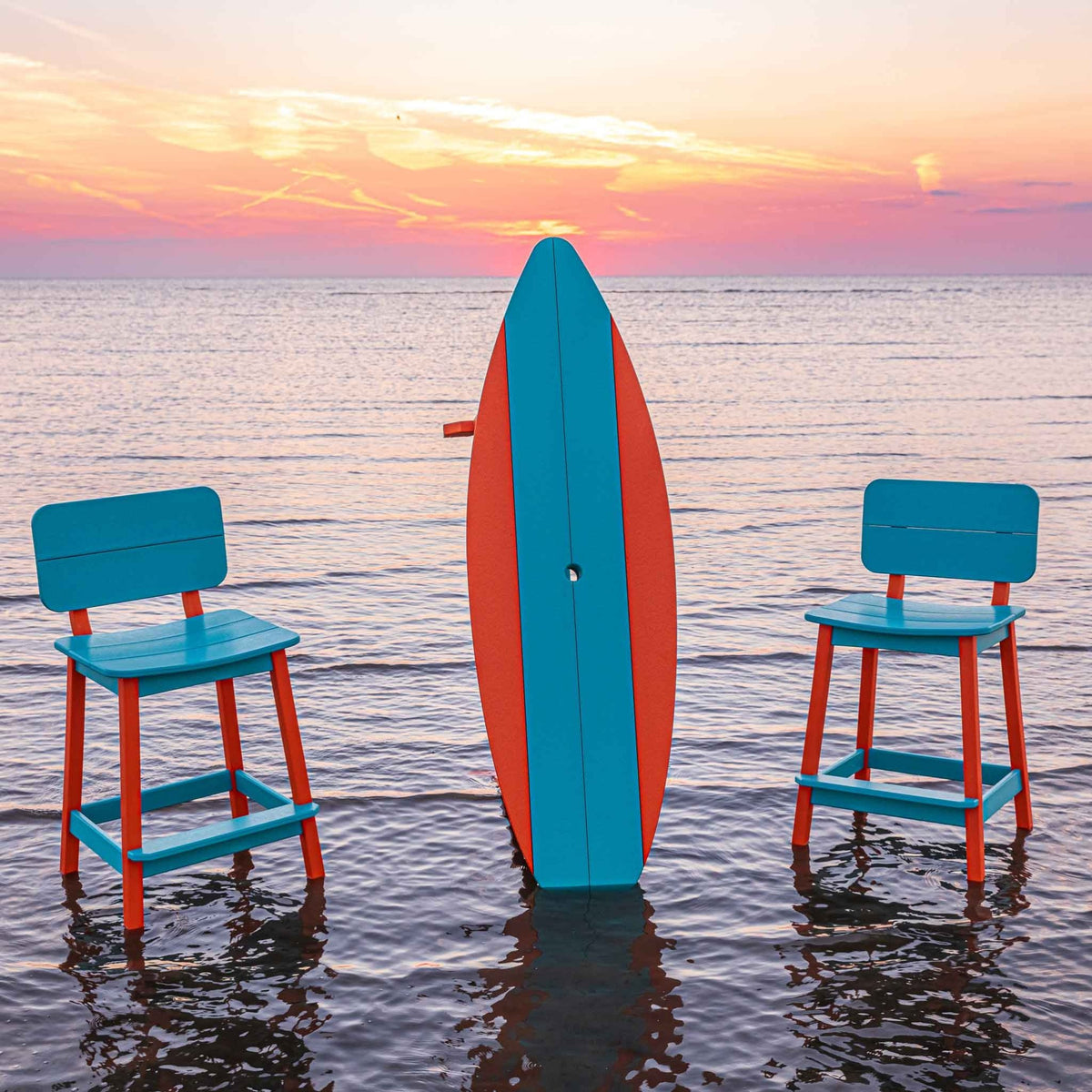 Two turquoise and orange poly bar stools flanking an upright surfboard table in the sunset surf
