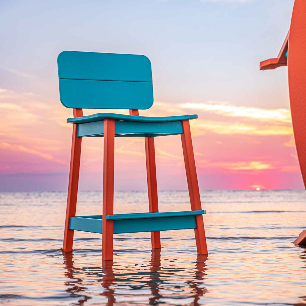 Low angle of an aqua and orange bar stool with the sun setting behind it over the ocean