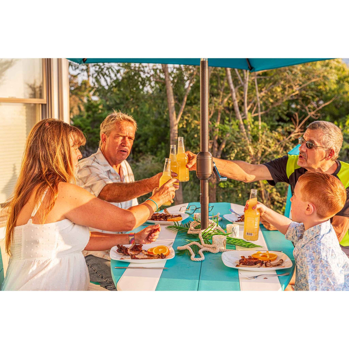 Family toasting bottles around a turquoise and white surfboard shaped bar table at golden hour