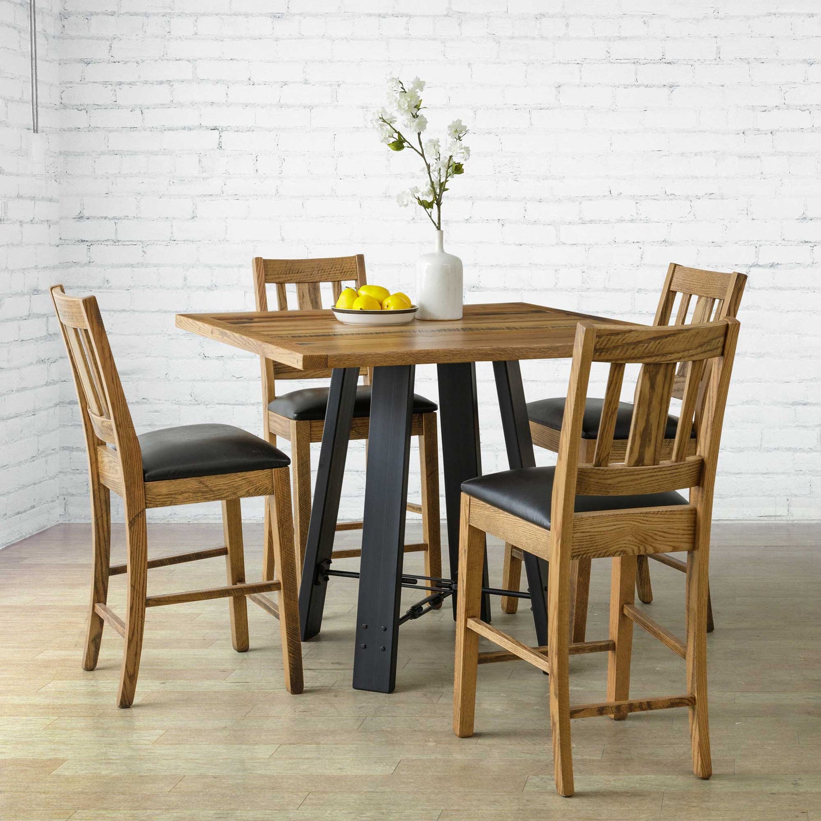Rustic counter table set with four black seat bar stools around a square reclaimed top in a white brick room