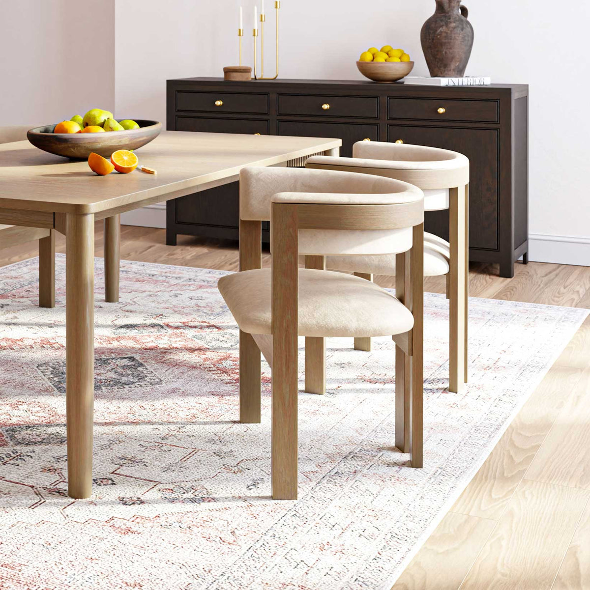 Cream upholstered barrel back dining chairs with light oak frames at a wood dining table with a dark sideboard behind
