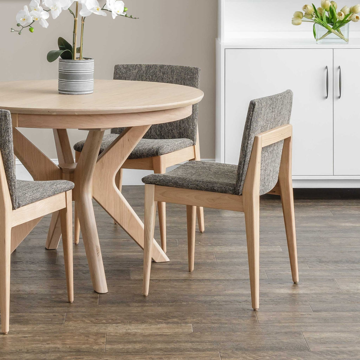 Maple dining chairs with charcoal tweed upholstery around a round light maple table in a white kitchen