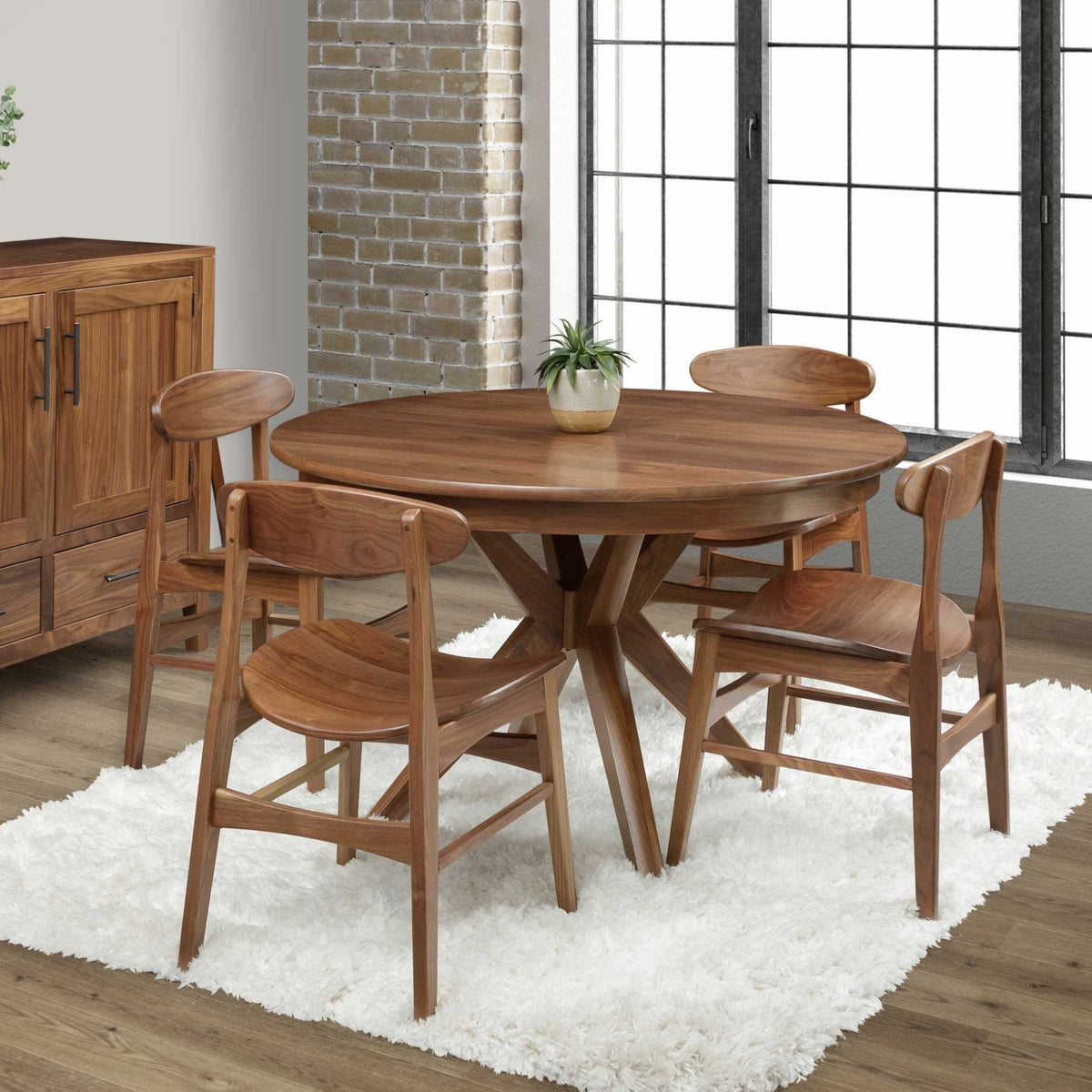 Round walnut pedestal dining table with a crossed splayed base and four curved back chairs on a white shag rug