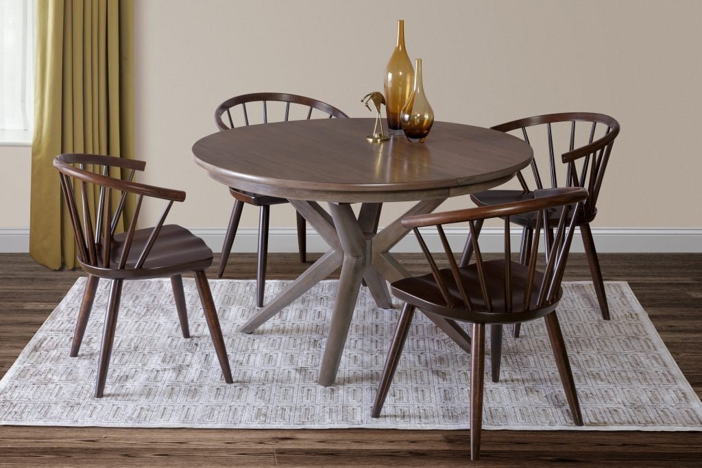 Round walnut dining table with a starburst base surrounded by four low spindle back arm chairs on a patterned rug
