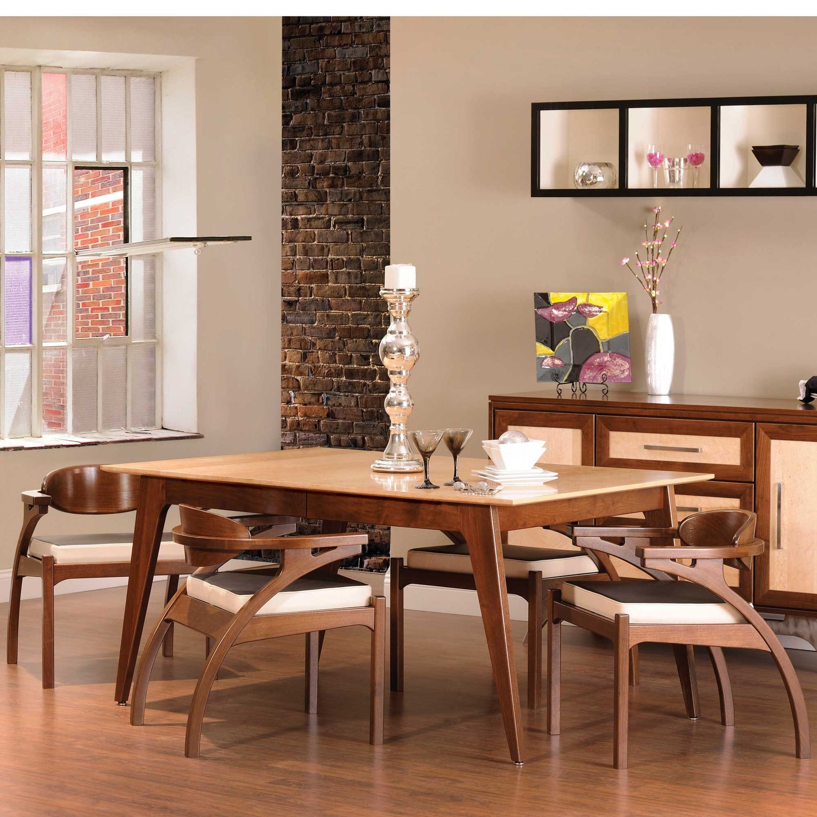 Mid century modern dining table with a maple top and walnut angled legs, set with curved arm chairs in a loft
