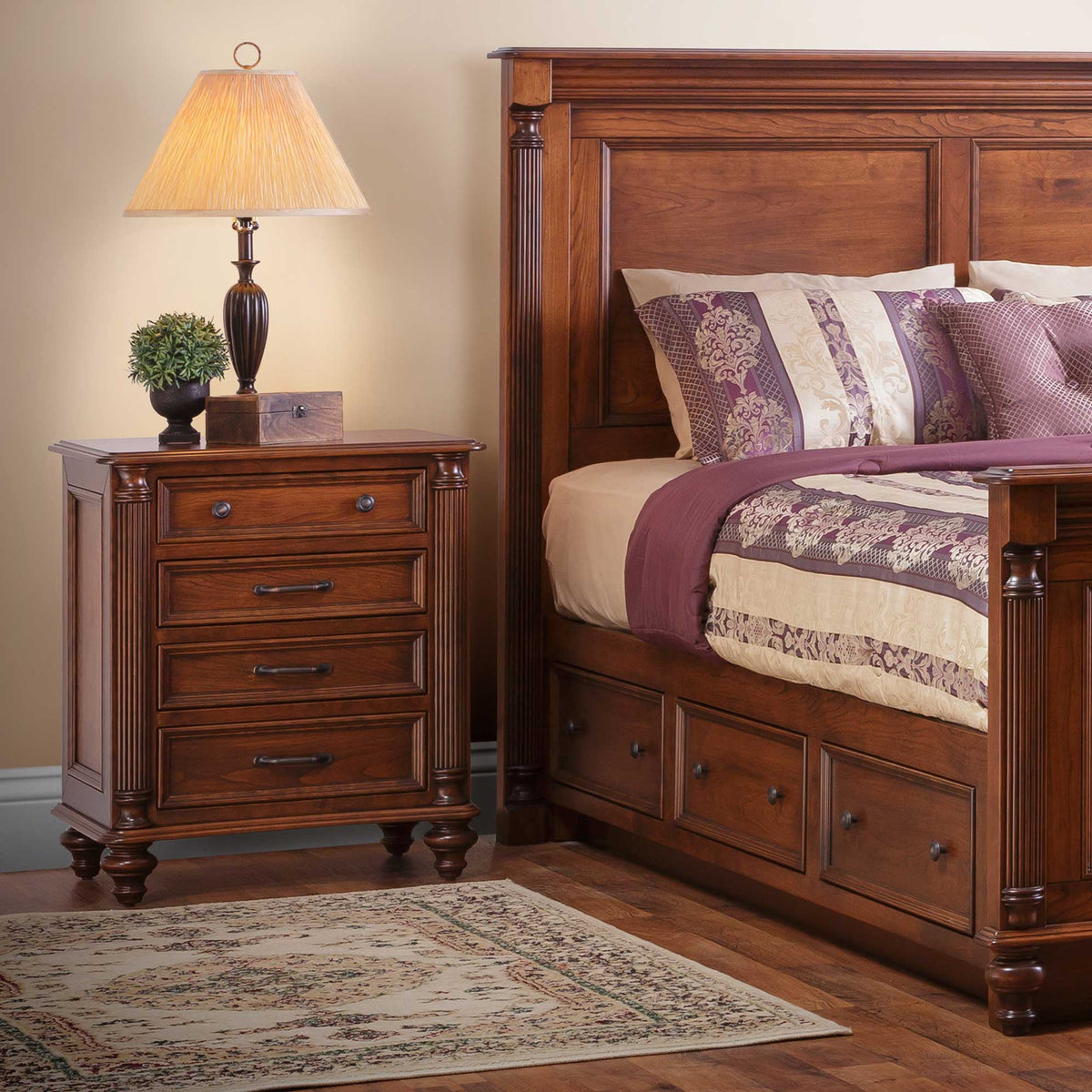 Four-drawer Milano bedside chest in cherry with bun feet and bronze bar pulls in a styled bedroom with lamp and area rug