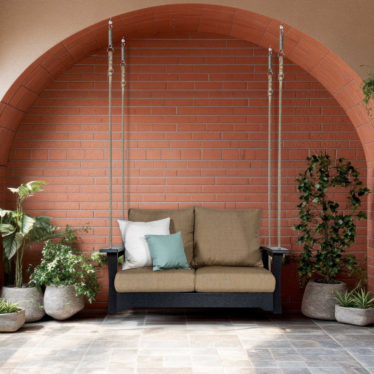 Black poly loveseat porch swing hung on cables with tan cushions under a brick archway with potted plants