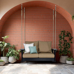 Black poly loveseat porch swing hung on cables with tan cushions under a brick archway with potted plants