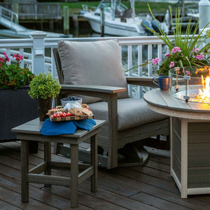 Driftwood poly swivel glider chair with tan cushions and side table of snacks by a glowing fire pit at a marina