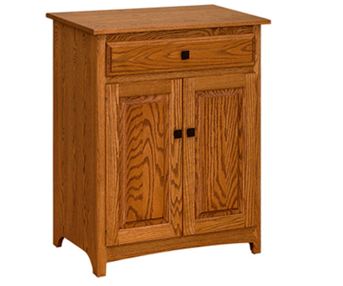 Oak microwave stand with a drawer and two paneled doors, holding a stainless microwave in a tiled oak kitchen