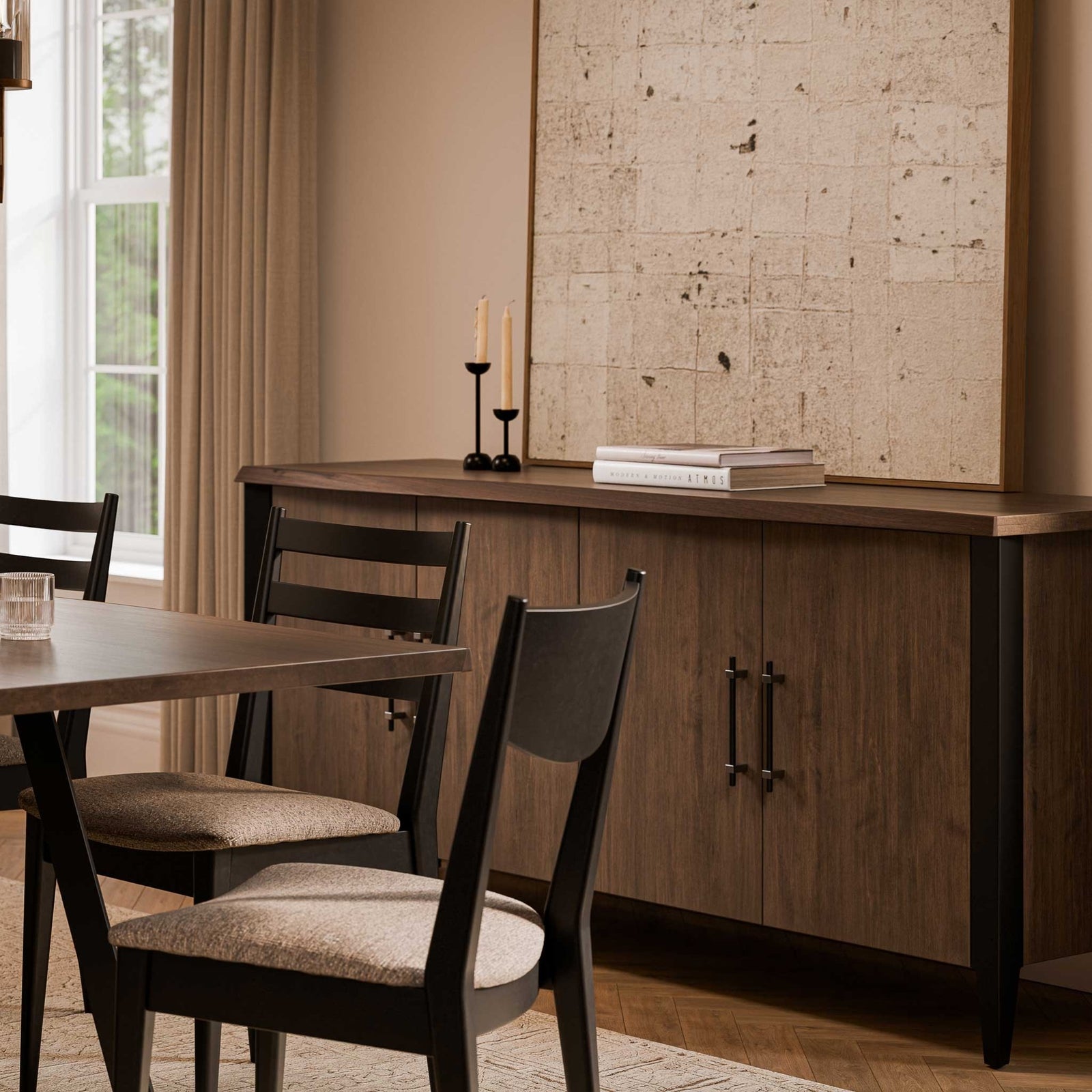 Walnut and black sideboard with four doors in a warm dining room with candlesticks and framed art above