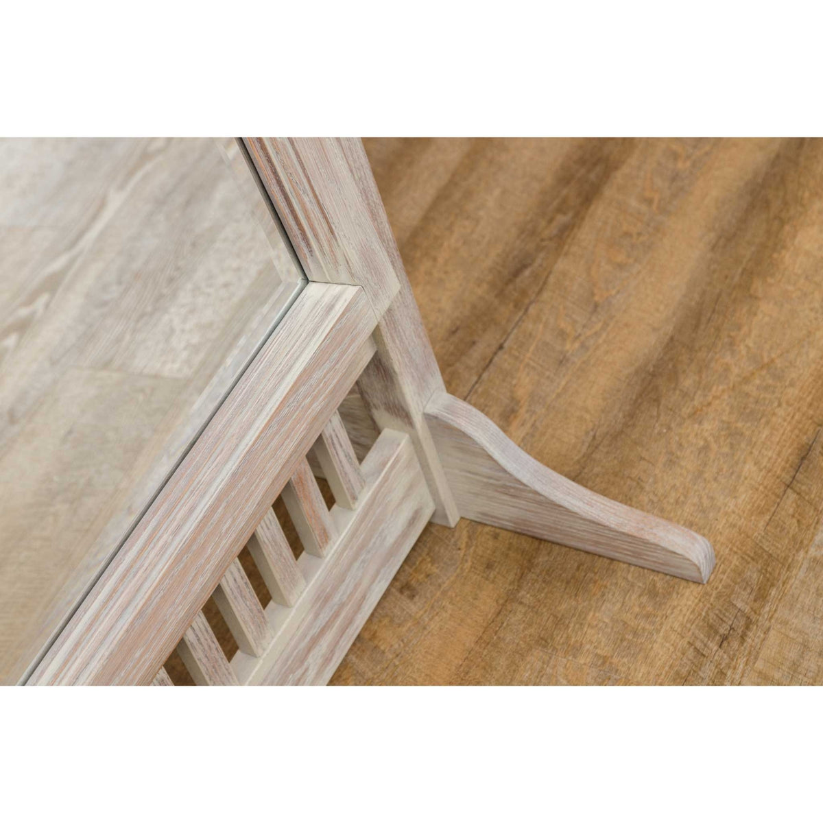 Close-up of the whitewashed cheval mirror's curved foot and slatted lower rail on a wood floor