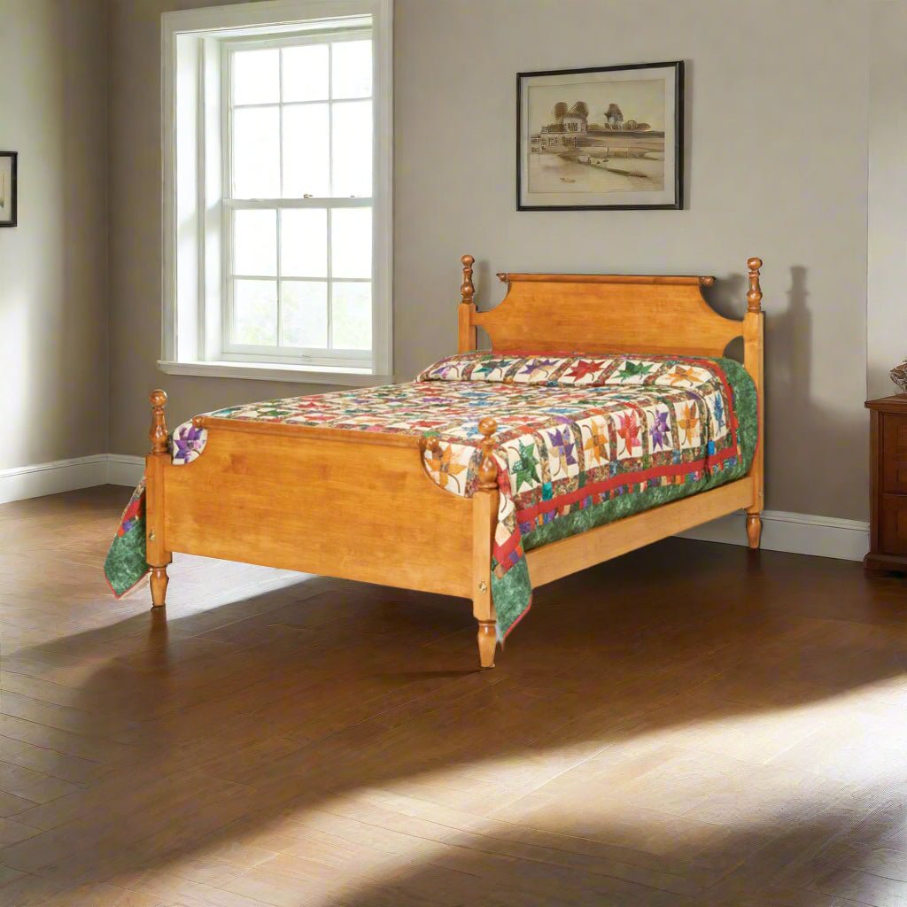 Colonial turned post bed in honey maple with a scroll headboard and low panel footboard, topped with a floral quilt