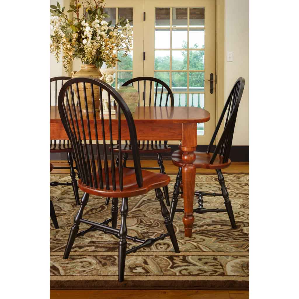 Black Windsor spindle chairs with cherry seats surrounding a cherry farmhouse table on a floral area rug