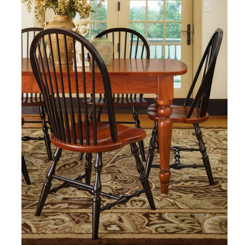 Black Windsor chairs with cherry saddle seats around a turned leg farmhouse table on a patterned rug