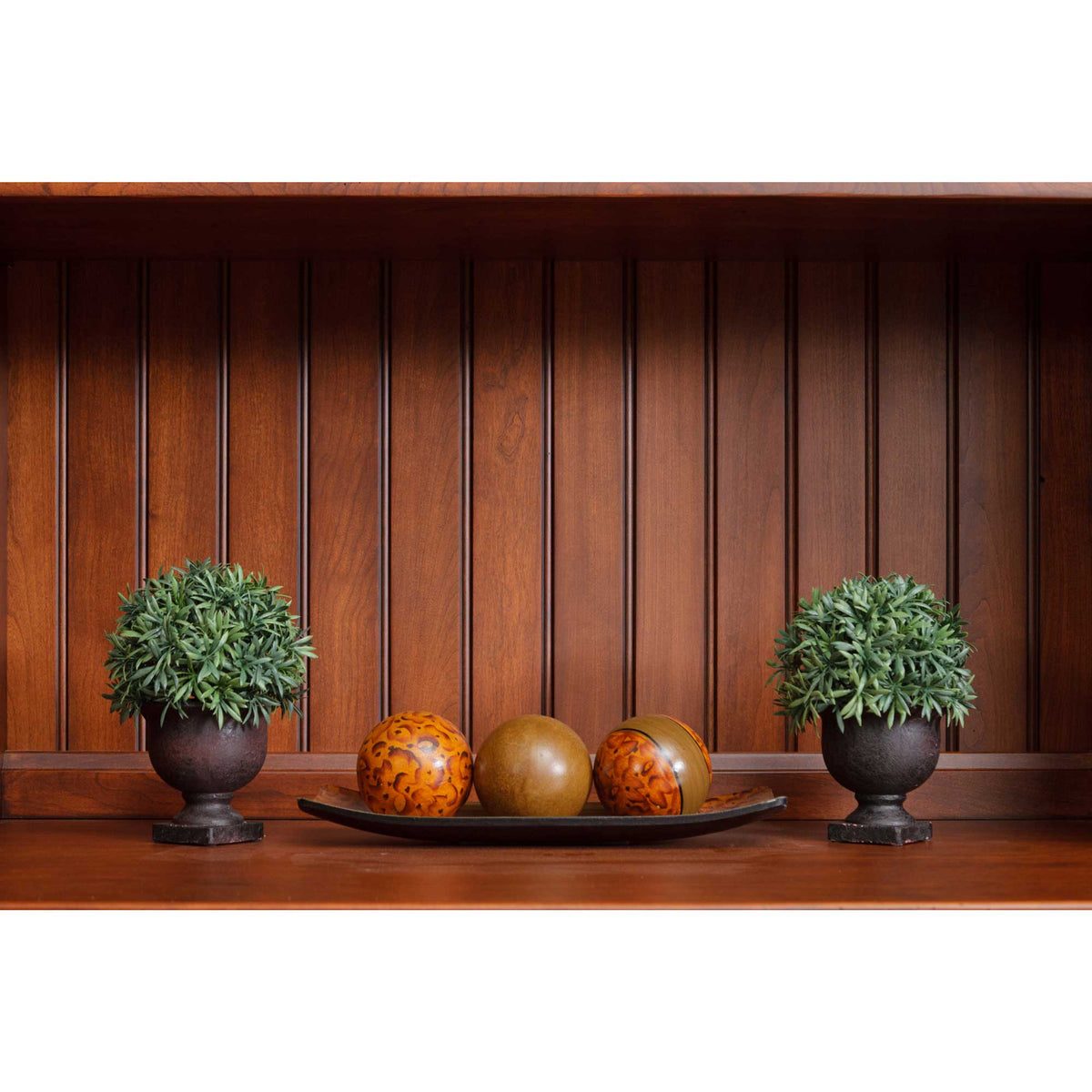 Beadboard backed hutch shelf styled with two topiary planters and a tray of decorative wooden spheres