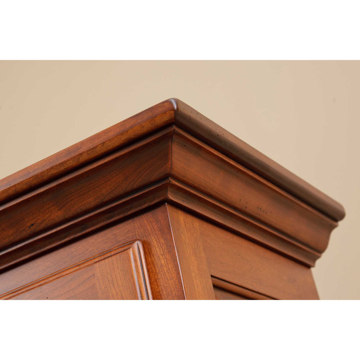 Close-up of the layered crown molding on the cherry hutch cabinet against a soft beige wall