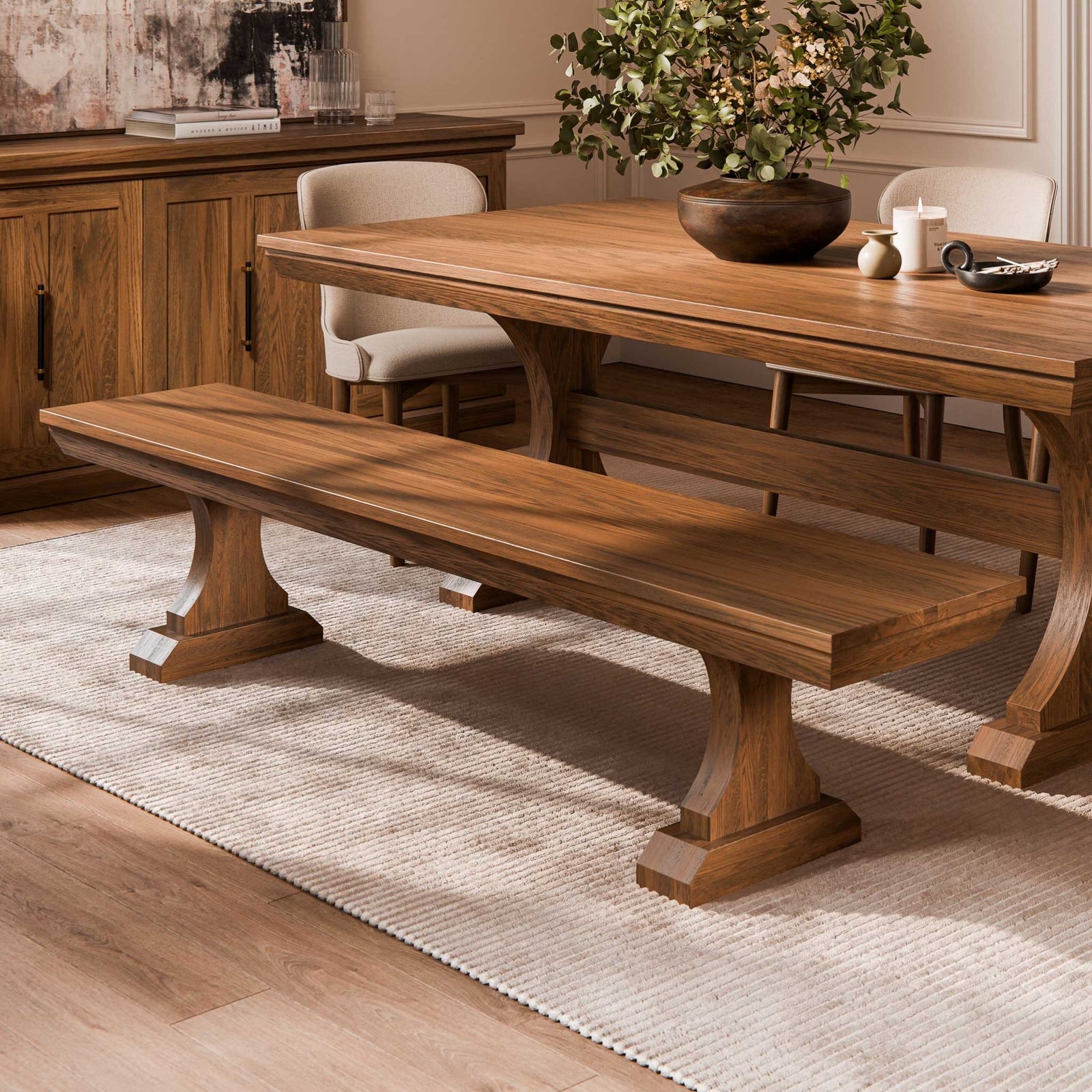 Walnut dining bench with a thick plank seat on two shaped pedestal legs beside a matching trestle table