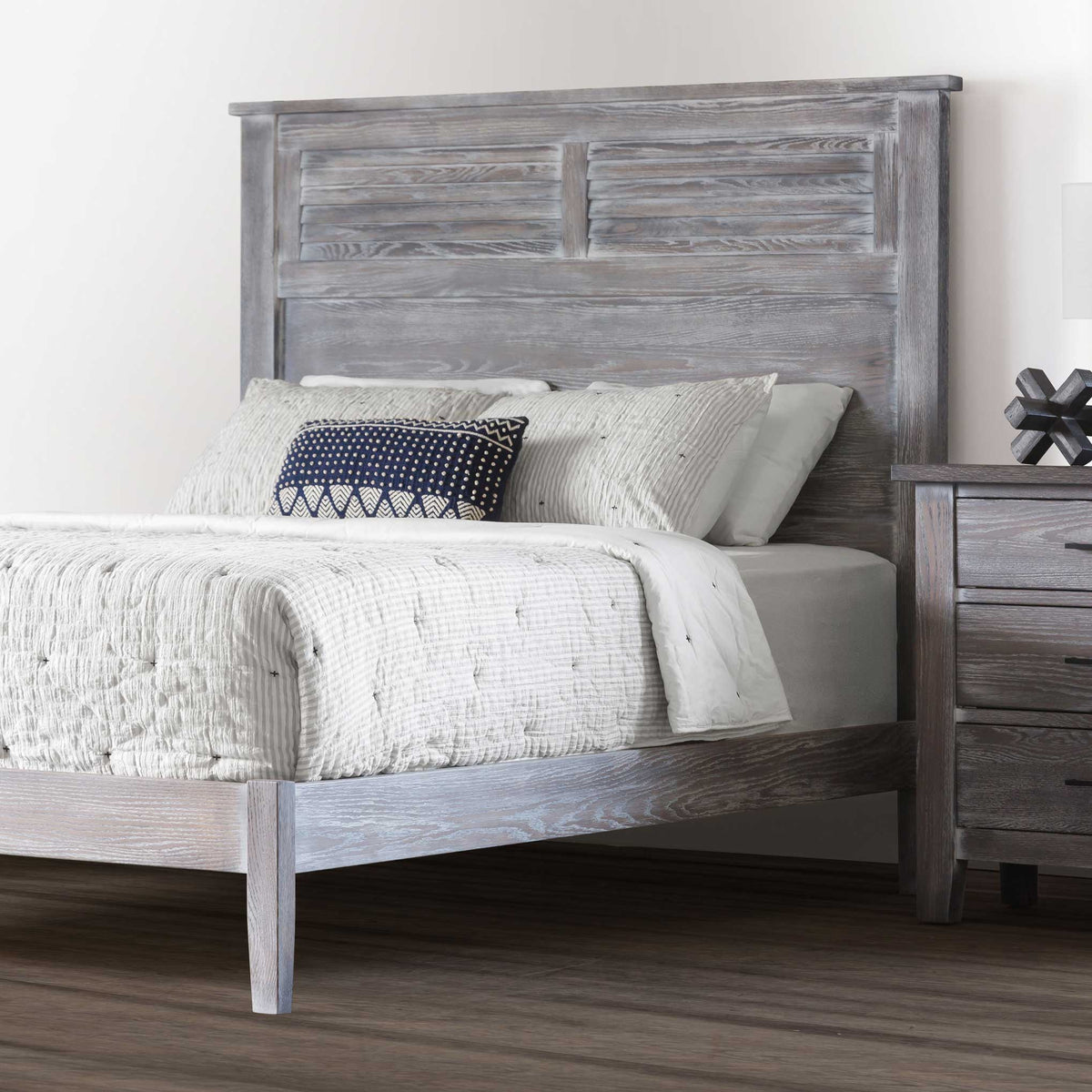 Rustic gray louver headboard with layered white bedding and a navy pillow beside a matching nightstand