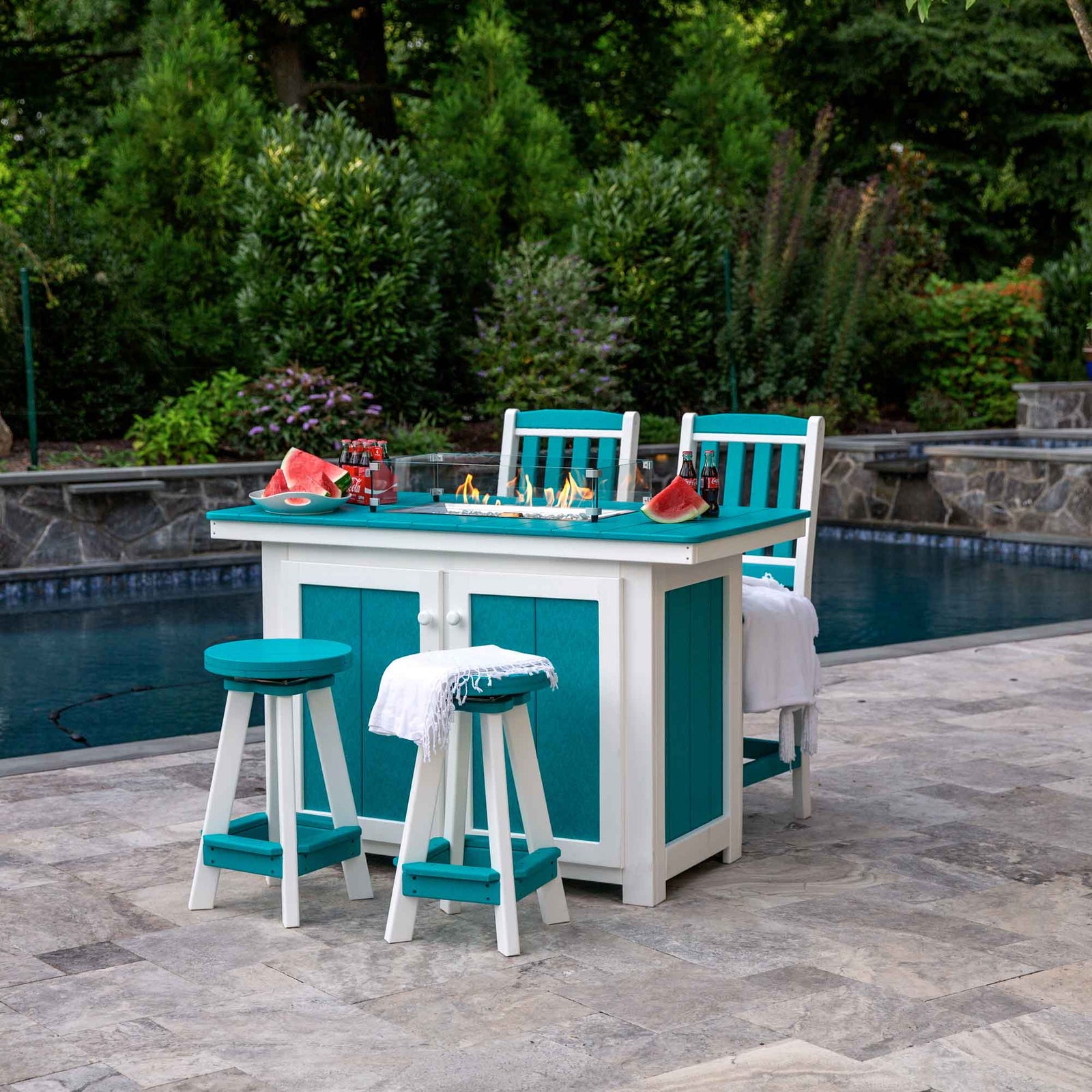 Aruba blue and white poly propane fire pit dining island with glass surround, two swivel stools and chairs by a pool