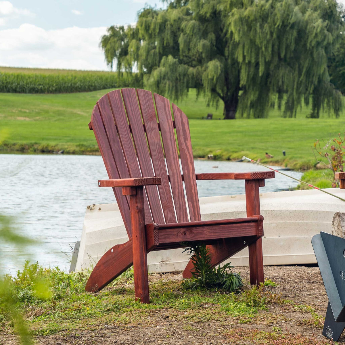 Cherry stained wood Adirondack chair with fan back slats and wide arms beside a pond and rowboat