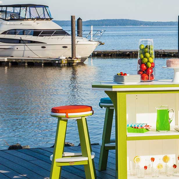 Orange and teal round stool cushions on green poly stools at a waterfront bar with a yacht behind