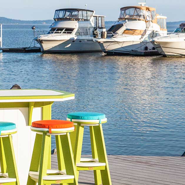 Lime green poly bar stools topped with turquoise and orange round cushions on a dock by moored boats