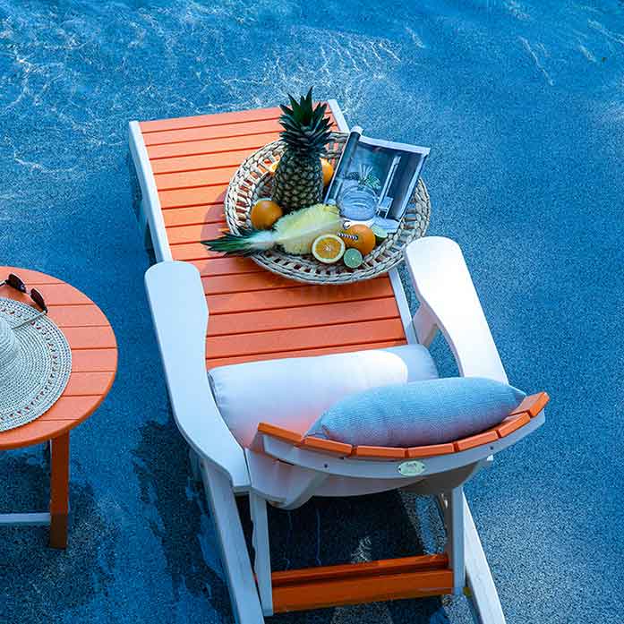 Overhead view of an orange and white poly chaise lounge with a white bolster and fruit tray by a pool
