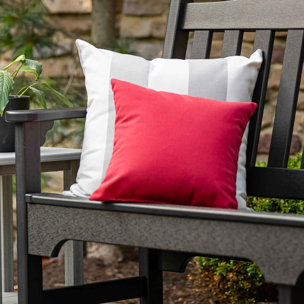 Red solid Sunbrella outdoor square pillow layered over a white striped pillow on a black poly lumber patio bench