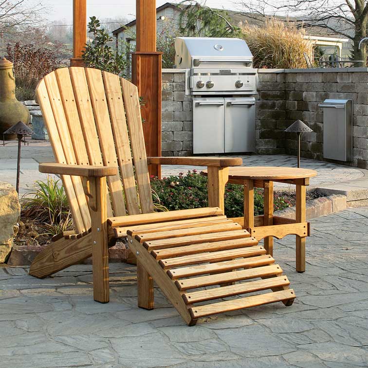 Natural wood Adirondack chair with a slatted pull out footrest and small side table on a flagstone patio near a grill