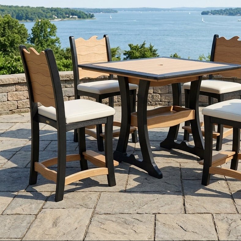 A 5-piece outdoor patio dining set with a square table and four chairs, featuring a black frame, natural wood slat backs and seats, and cream cushions, set on a stone patio overlooking a scenic lake.