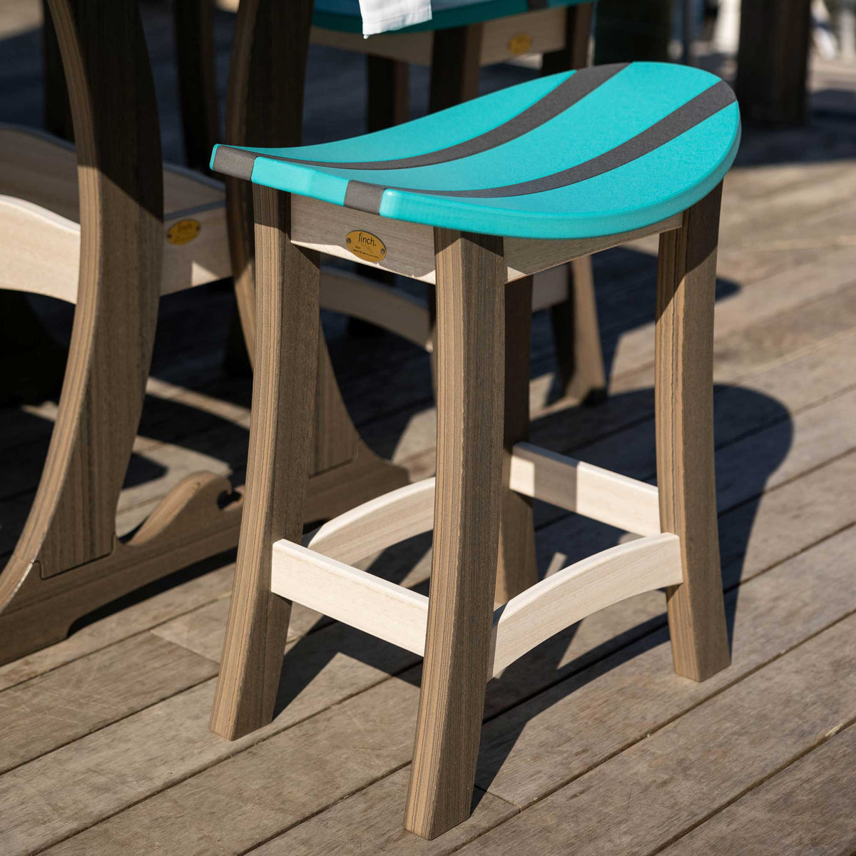 Teal and gray striped saddle stool with weatherwood splayed legs and footrest on a sunny dock