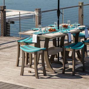 Weatherwood poly bar table with aruba blue saddle stools set with plates and food on a dock beside the water