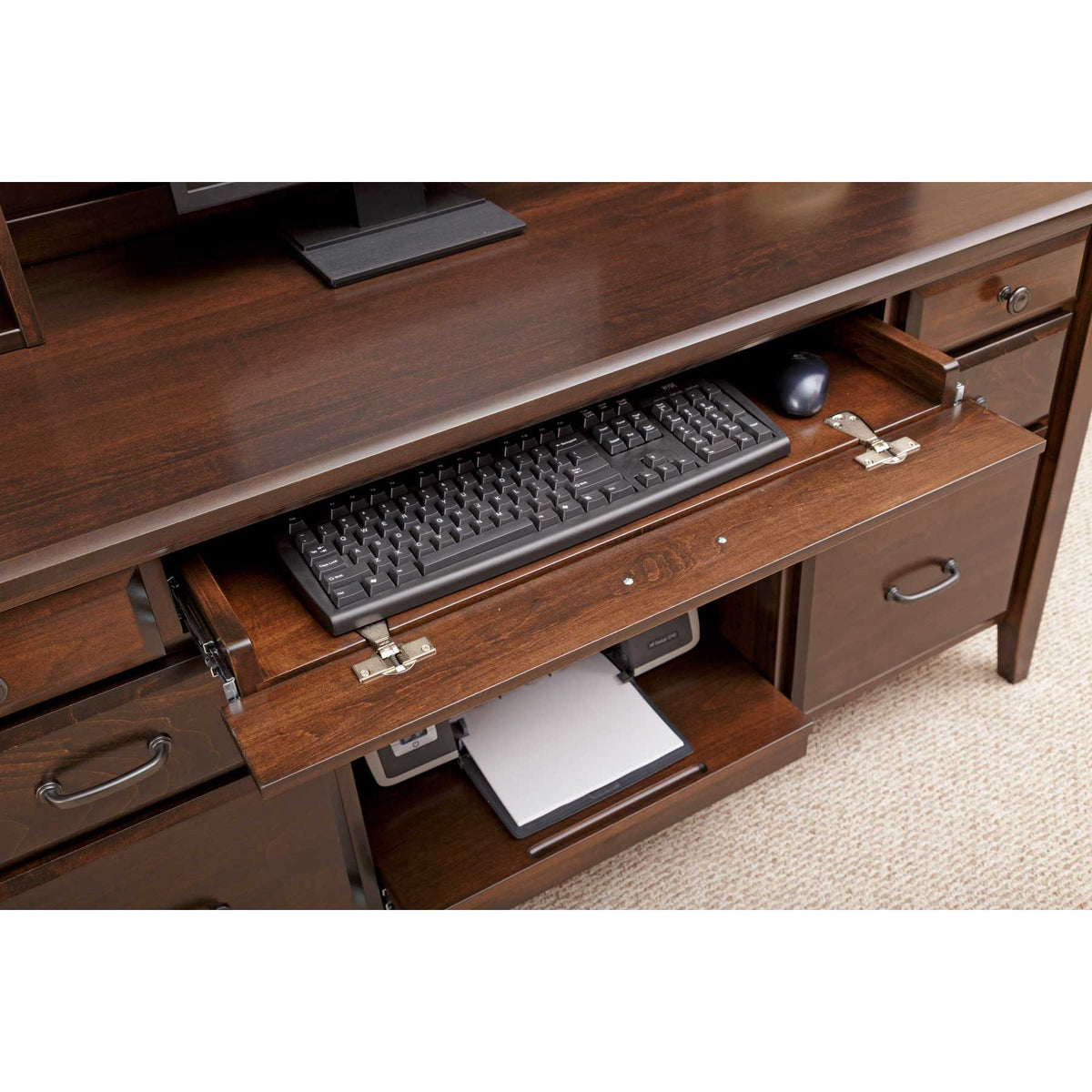 Keyboard tray extended under the desk top with a black keyboard and mouse above the printer shelf