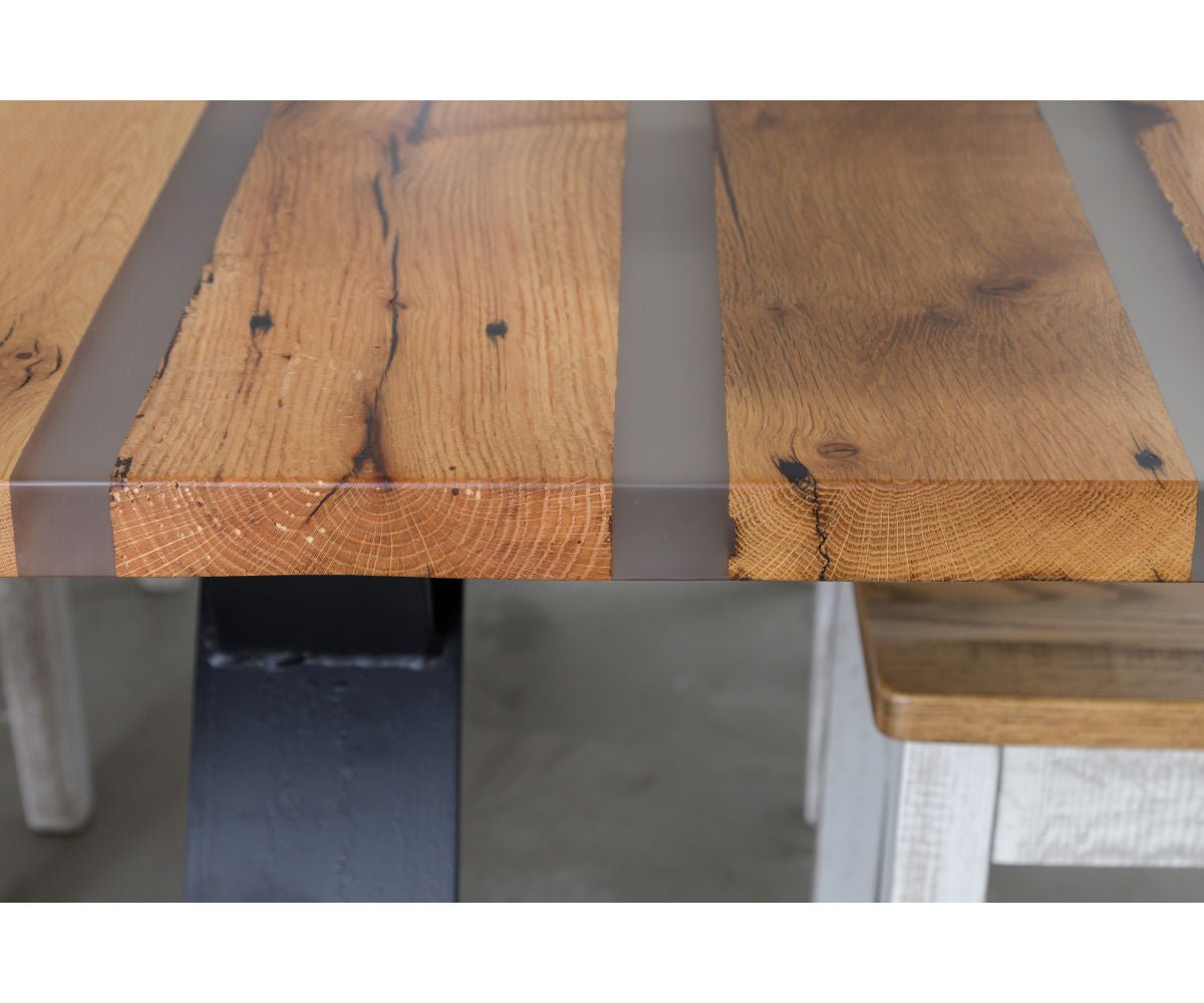 Side edge view of the reclaimed oak and gray resin dining table top above its black metal trestle leg