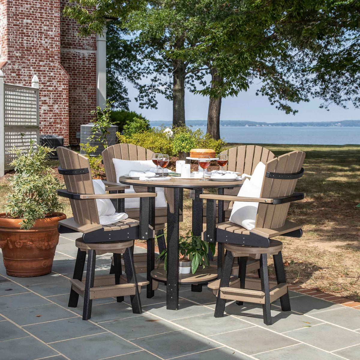 Weatherwood and black poly round bar table with four swivel Adirondack bar chairs and pillows on a flagstone patio