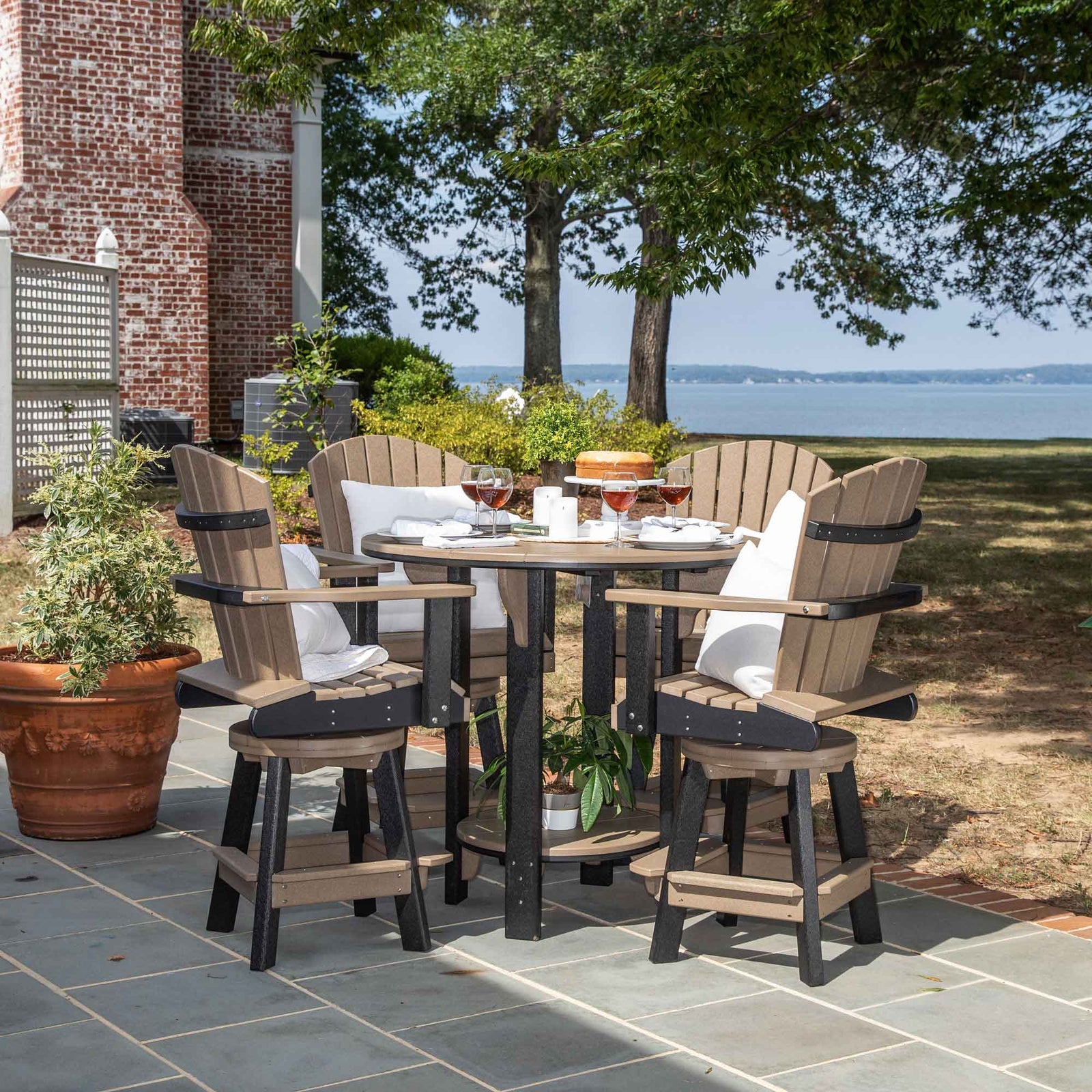 White poly 42 inch round bar height patio table with four swivel Adirondack chairs set for a party on a bay deck