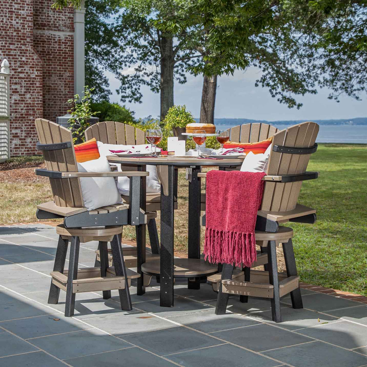 Tan and black poly round bar height patio set for four with swivel chairs, throw and cake by a lawn and bay