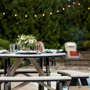 Table setting on a round weatherwood poly picnic table with flowers and blue napkins under patio string lights