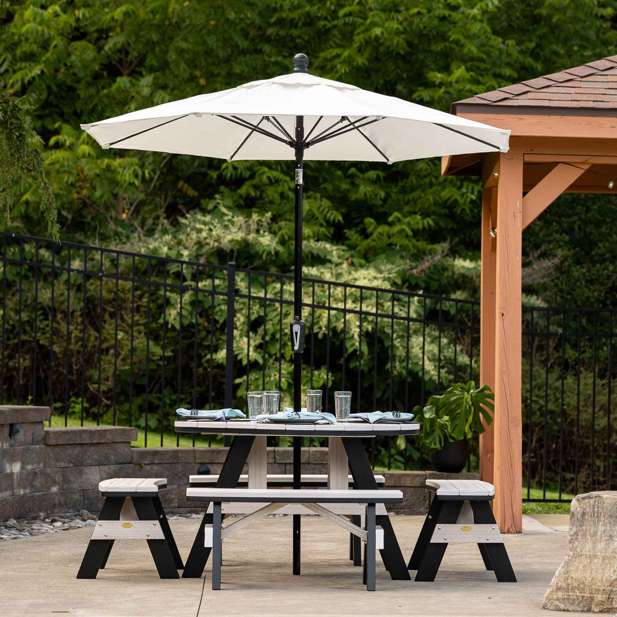 Round poly patio garden table for four with cream top and black frame, set with plates under a patio umbrella