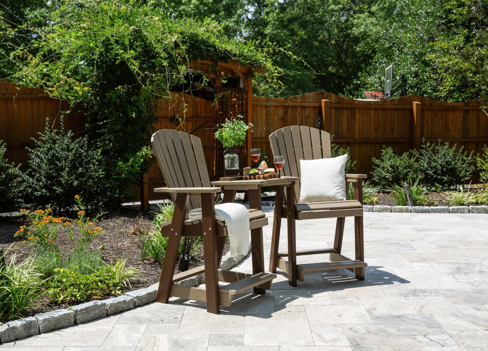 Two brown and weatherwood poly counter height chairs joined by a small center table on a travertine patio