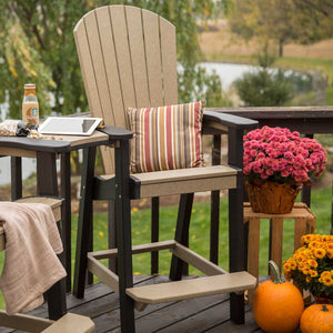 Weatherwood and black tall Adirondack chair on a deck with a striped pillow, mums and pumpkins in autumn