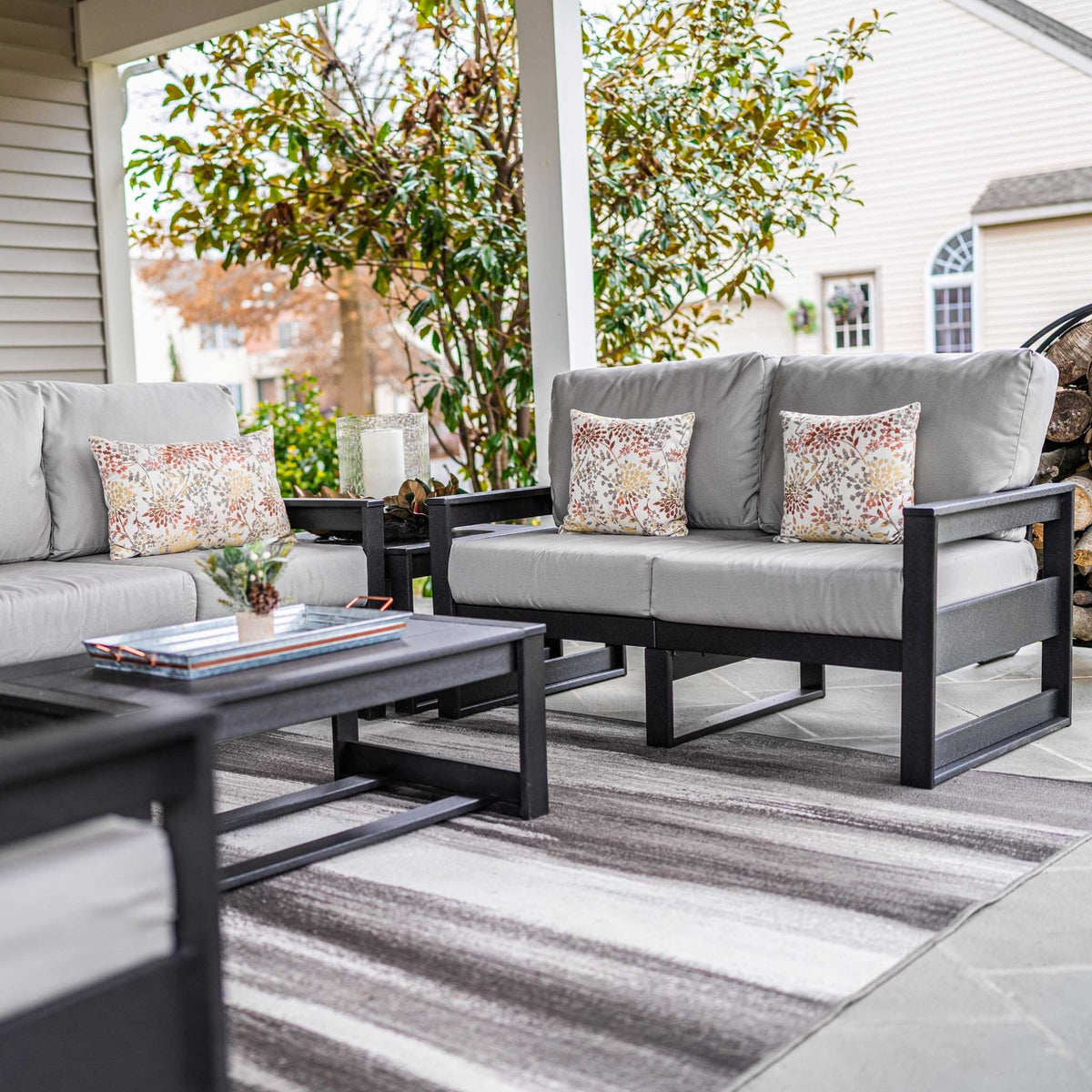 Black poly loveseats with gray cushions and floral pillows facing a coffee table on a covered porch