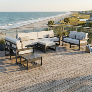 Gray poly patio set with white cushions including a four-seat sofa, two loveseats and ottoman on a beach deck